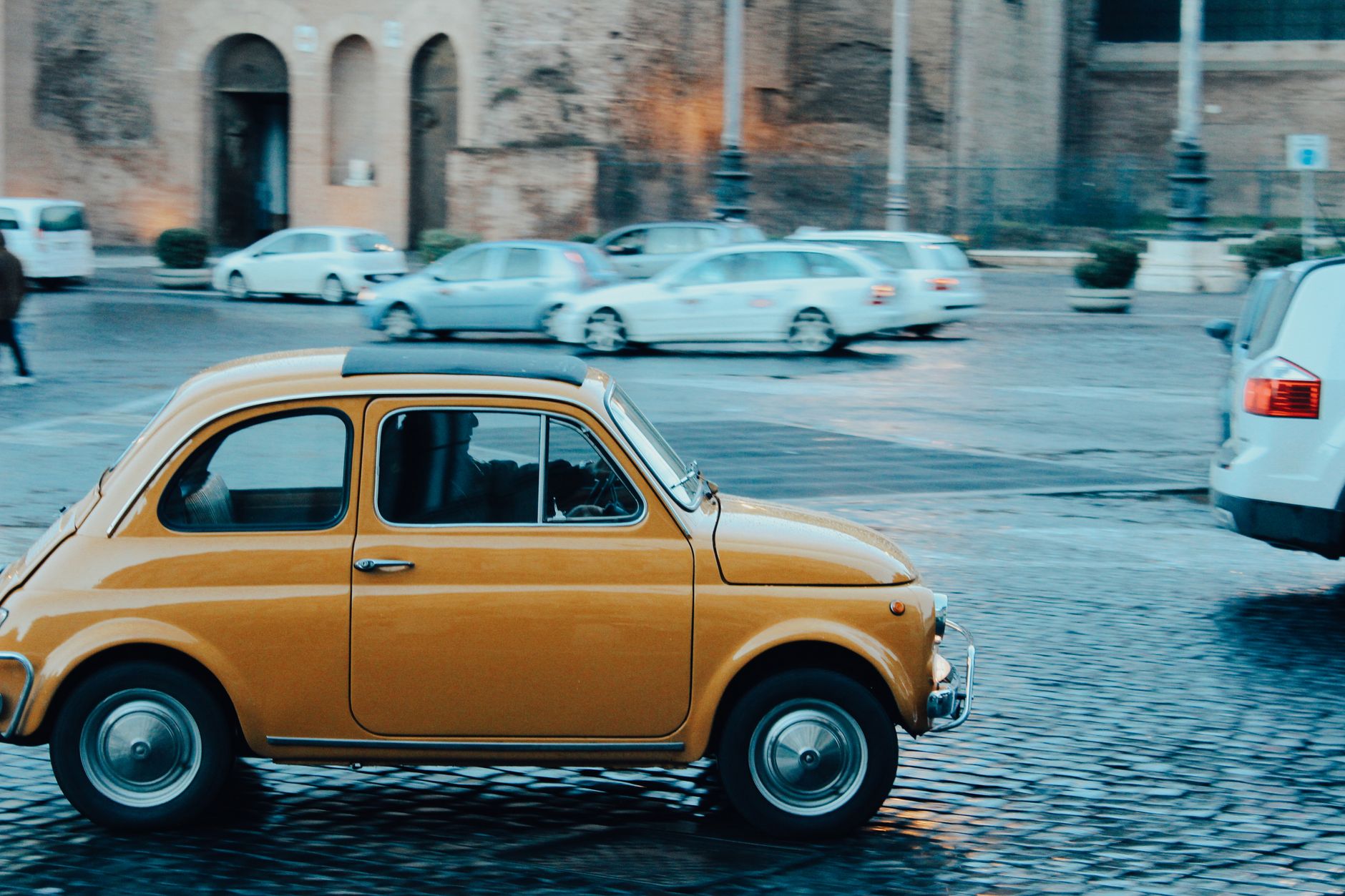 Żółty Fiat 500 jedzie po brukowanej ulicy w Rzymie